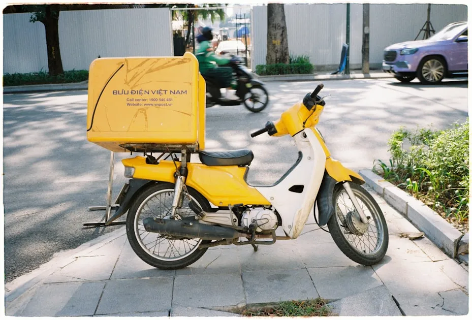 Yellow delivery motorcycle parked on sidewalk — Cách Tính Phí Gửi Hàng Viettel Post - Công Thức Chi Tiết 2026