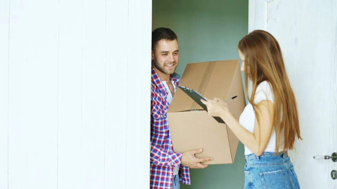 Young man deliver cardboard box to customer at home. Woman signing in clipboard for receiving parcel — Mẹo Gửi Hàng Online...